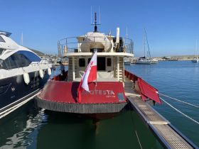 A view of the 'APOTESTA' boat docked in a marina, showcasing its unique design and surroundings. Perfect for exploring coastal destinations.