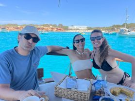 A joyful group of friends enjoys drinks on a boat, surrounded by stunning turquoise waters — perfect for a fun day out on the sea.