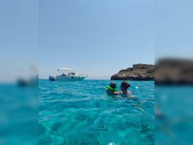 A mother and child enjoy a refreshing swim in crystal-clear waters, with a boat anchored nearby — a perfect family day out on the water.