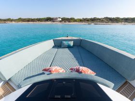 A cozy lounge area on a boat featuring plush seating and decorative pillows, perfect for relaxing while enjoying the stunning turquoise waters.