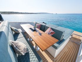 A beautifully designed interior seating area on a boat, featuring a wooden table and plush cushions, perfect for dining or relaxing while enjoying the stunning ocean views.