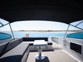 A stylish interior view of a boat's lounge area, featuring comfortable seating and a table, perfect for relaxing while enjoying the scenic turquoise waters.