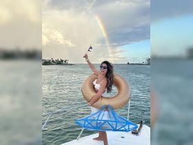A joyful woman celebrates on a boat with a rainbow in the background, showcasing a fun day on the water with a float and vibrant atmosphere.