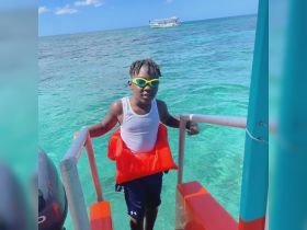 A young boy in a life jacket poses at the edge of a boat, ready to enjoy the clear turquoise waters — a perfect moment for family fun on the ocean.
