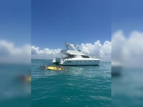 A lively group enjoys a fun day in the water, swimming and playing on a yellow float near a stylish yacht, perfect for summer adventures and group outings.