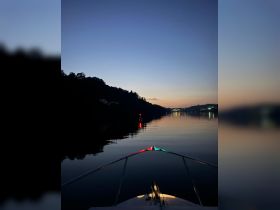 A serene view from the bow of a boat at dusk, showcasing calm waters and a picturesque sunset — perfect for evening cruises.