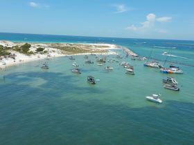 A vibrant scene of boats anchored near a sandy beach, with people enjoying the sun and water — a perfect sandbar stop for fun and relaxation.