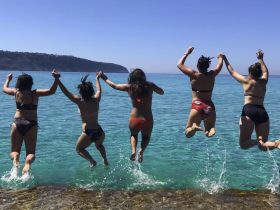 A group of friends joyfully jumps into the crystal-clear waters, capturing the essence of summer fun and adventure by the beach.