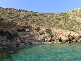 A group enjoys a sunny day at the beach, with activities like swimming and kayaking in the clear waters — a perfect spot for relaxation and fun.