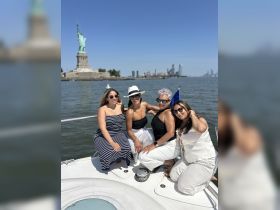 A joyful group of friends poses on a boat with the iconic Statue of Liberty in the background, capturing a memorable moment on the water.