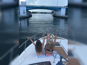 A joyful moment as two women, including a child, celebrate on the bow of a boat while passing under a bridge — a perfect snapshot of fun on the water.