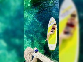 A woman enjoys a sunny day paddleboarding on crystal-clear waters, perfect for relaxation and water activities.