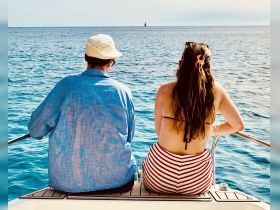A couple enjoys a serene moment on the deck of a boat, gazing out at the tranquil ocean and distant sailboat — perfect for romantic getaways or peaceful retreats on the water.