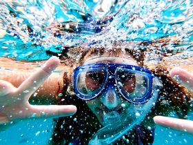 A joyful child snorkels underwater, flashing a peace sign amidst bubbles — a perfect snapshot of fun and adventure in the water.