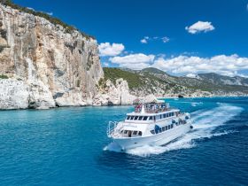 A scenic view of a boat cruising through turquoise waters, surrounded by stunning cliffs and a lively group of passengers enjoying the journey.