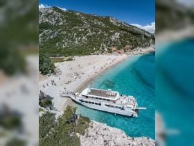 A stunning aerial view of a boat anchored near a beautiful beach, with people enjoying the sun and turquoise waters — perfect for island hopping adventures.