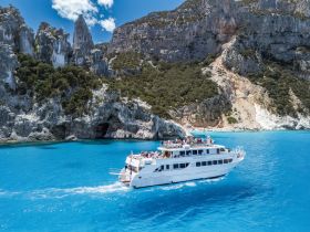 A stunning aerial view of a cruise boat navigating through crystal-clear waters, surrounded by dramatic cliffs and lush greenery — an ideal setting for unforgettable coastal adventures.