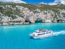 An aerial view of a lively boat cruising through stunning turquoise waters, surrounded by dramatic cliffs — a perfect scene for group adventures and scenic tours.