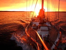 A stunning sunset view from a sailboat, showcasing the vessel's elegant lines against a vibrant orange sky — perfect for romantic evening cruises.