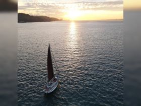 A stunning aerial view of a sailboat gliding through calm waters at sunset, showcasing the beauty of sailing and the tranquility of the sea.