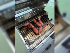 Delicious sausages grilling on a boat barbecue, perfect for a day of fun on the water. Enjoy tasty meals while cruising or anchored.