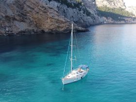 A stunning aerial view of a sailboat navigating through crystal-clear turquoise waters, surrounded by dramatic cliffs — perfect for showcasing sailing adventures in picturesque locations.