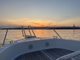 A serene view from the front of a yacht at sunset, showcasing calm waters and a picturesque sky — perfect for evening cruises.