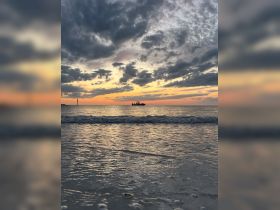 A picturesque sunset view with a boat silhouetted against the vibrant sky, capturing the serene beauty of a beach evening.