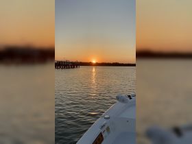 A serene sunset view from the bow of a boat, showcasing the tranquil waters and a distant dock — perfect for peaceful evening cruises.