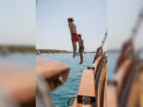 Two friends leap off the side of a boat into the clear blue waters, capturing the essence of summer fun and adventure on the water.