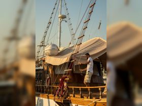 A crew member adjusts the rigging on a beautiful sailing vessel during sunset, showcasing the intricate details of the boat and the art of sailing.