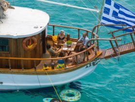 A lively group enjoys a meal aboard a beautiful boat, surrounded by turquoise waters — perfect for memorable gatherings and celebrations on the sea.