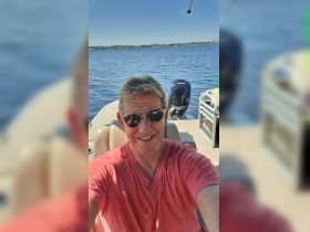 A man enjoys a sunny day on the water, capturing a selfie aboard a boat — perfect for showcasing fun boating adventures.
