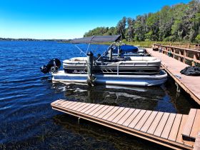 A sleek pontoon boat docked by the shore, surrounded by calm waters and lush greenery, perfect for leisurely outings on the water.