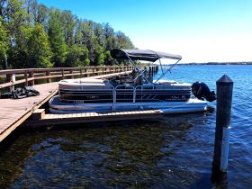 A sleek pontoon boat is docked at a wooden pier, surrounded by serene waters and lush greenery, perfect for leisurely outings on the lake.