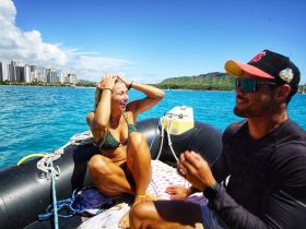 A joyful moment on the water as a woman and man share laughter aboard a boat, with stunning ocean views and city skyline in the background — perfect for capturing the spirit of adventure.