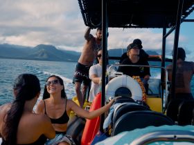 A joyful group enjoys a boat ride, laughing and sharing moments on the water, surrounded by stunning ocean views and mountains — perfect for adventure seekers.