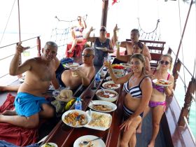 A lively group enjoys a festive meal aboard a boat, raising drinks and sharing delicious food — perfect for a memorable boat party experience.