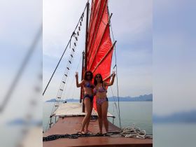 Two friends pose joyfully aboard a sailing boat with vibrant red sails, capturing a fun moment on the water — perfect for adventure seekers and sailing enthusiasts.