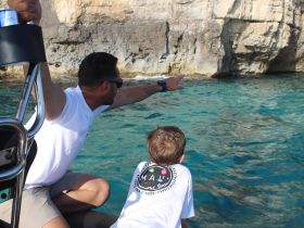 A man and a child point towards the rocky coastline while enjoying a boat trip, highlighting the excitement of exploring beautiful marine landscapes together.