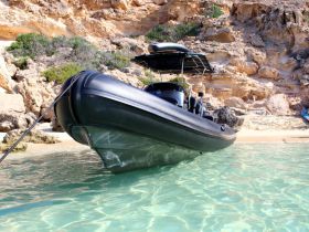 A sleek speedboat anchored in crystal-clear waters, showcasing its design against a stunning rocky backdrop — perfect for exploring coastal destinations.
