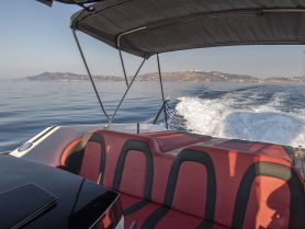 A view of the comfortable seating area inside a boat, showcasing the helm and a serene backdrop of calm waters and distant hills.