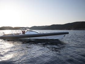 A sleek speedboat glides through calm waters, showcasing its elegant design against a serene backdrop of hills and sunset.