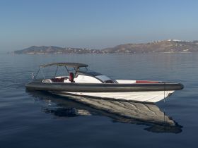 A sleek speedboat glides through calm waters, showcasing its elegant design against a serene backdrop of distant hills.
