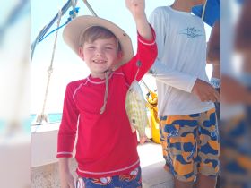 A young boy proudly displays his catch while fishing on a boat, capturing the joy of a family fishing adventure at sea.
