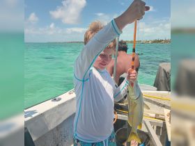 A young boy proudly holds up his catch while fishing on a boat, showcasing the joy of a successful day on the water.