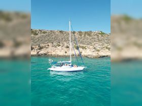 A lively group enjoys a sailing adventure on a beautiful day, surrounded by stunning turquoise waters and rocky cliffs.