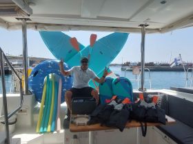 A crew member showcases a variety of water toys and safety gear on board, including paddleboards and life jackets, perfect for a fun day on the water.