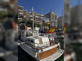 A beautifully docked boat named 'Nostromo 1' showcases its elegant design against a backdrop of modern buildings and clear blue skies, perfect for a day on the water.