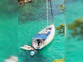 A person paddleboards near a sailboat in stunning turquoise waters, showcasing a perfect day of adventure on the water.